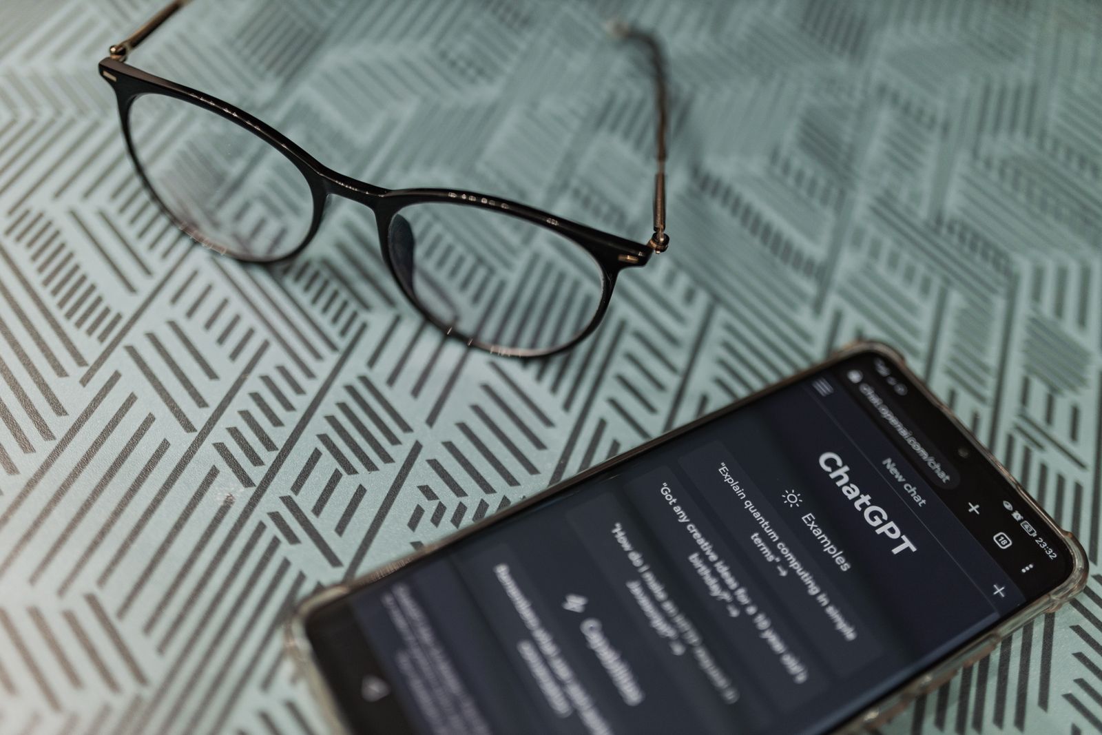 A patient holding a phone open to an AI chatbot next to a pair of reading glasses, the way people research a medical practice at night