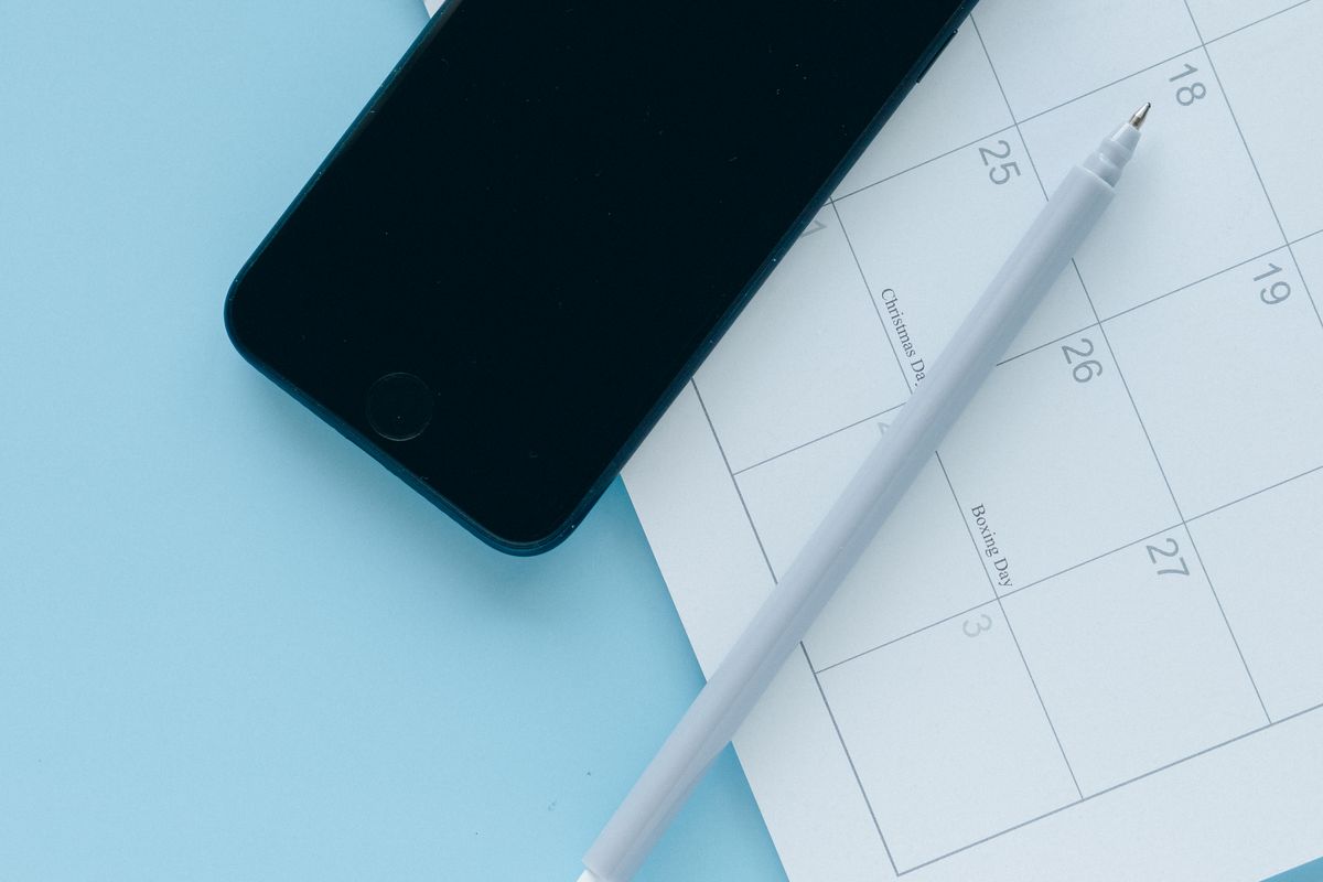 A phone resting on a paper calendar with a pen, showing the choice between real time online booking and a manual request an appointment form for a medical practice