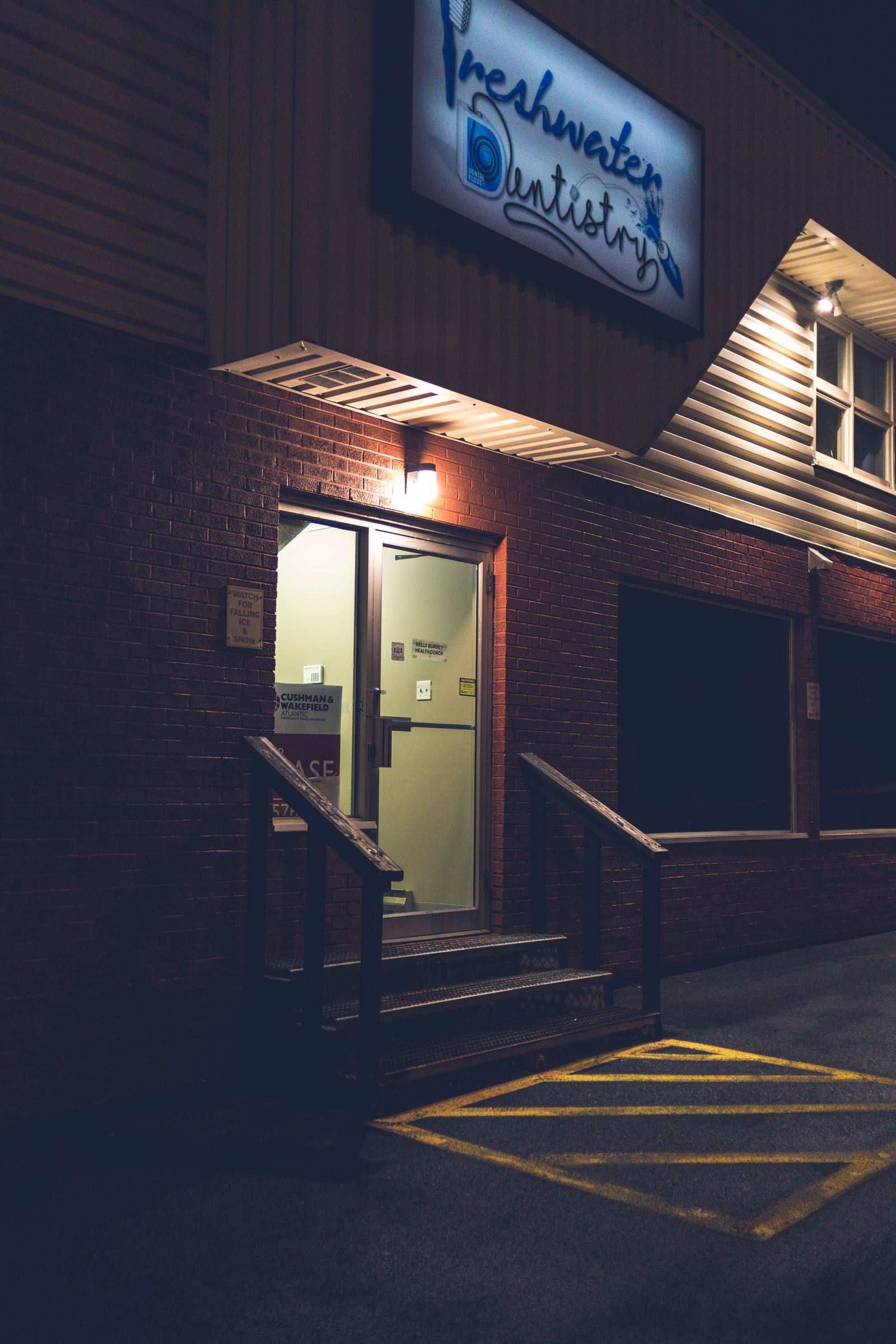 A lit dental practice sign above a clinic entrance at night, the moment a practice name becomes the first thing patients see and search for