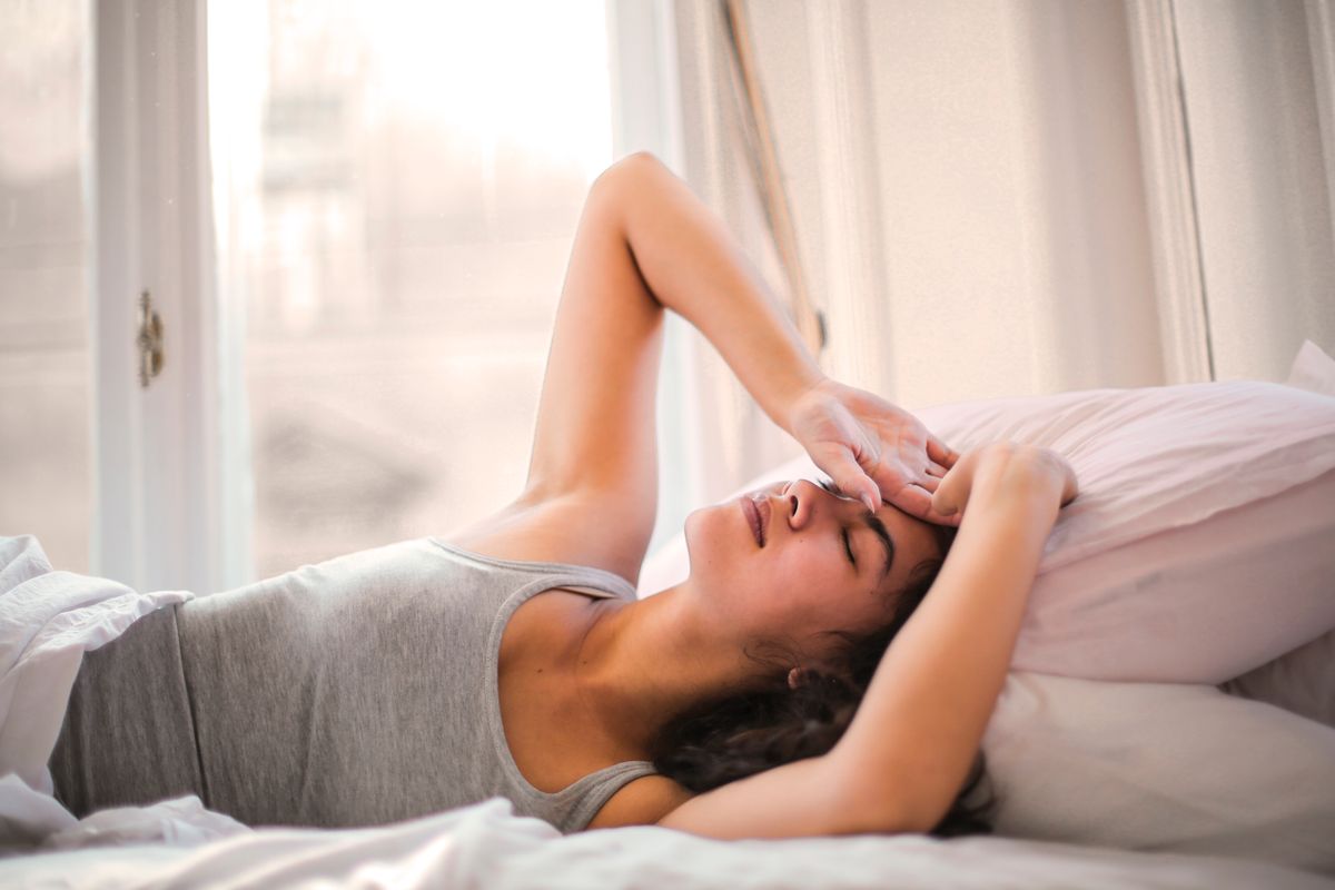 A woman lying in bed feeling unwell, the moment a patient reaches for their phone to check symptoms before booking a doctor