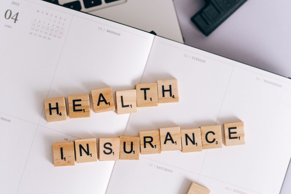 Health insurance spelled in letter tiles on a planner next to a laptop, representing insurance messaging in medical practice ads