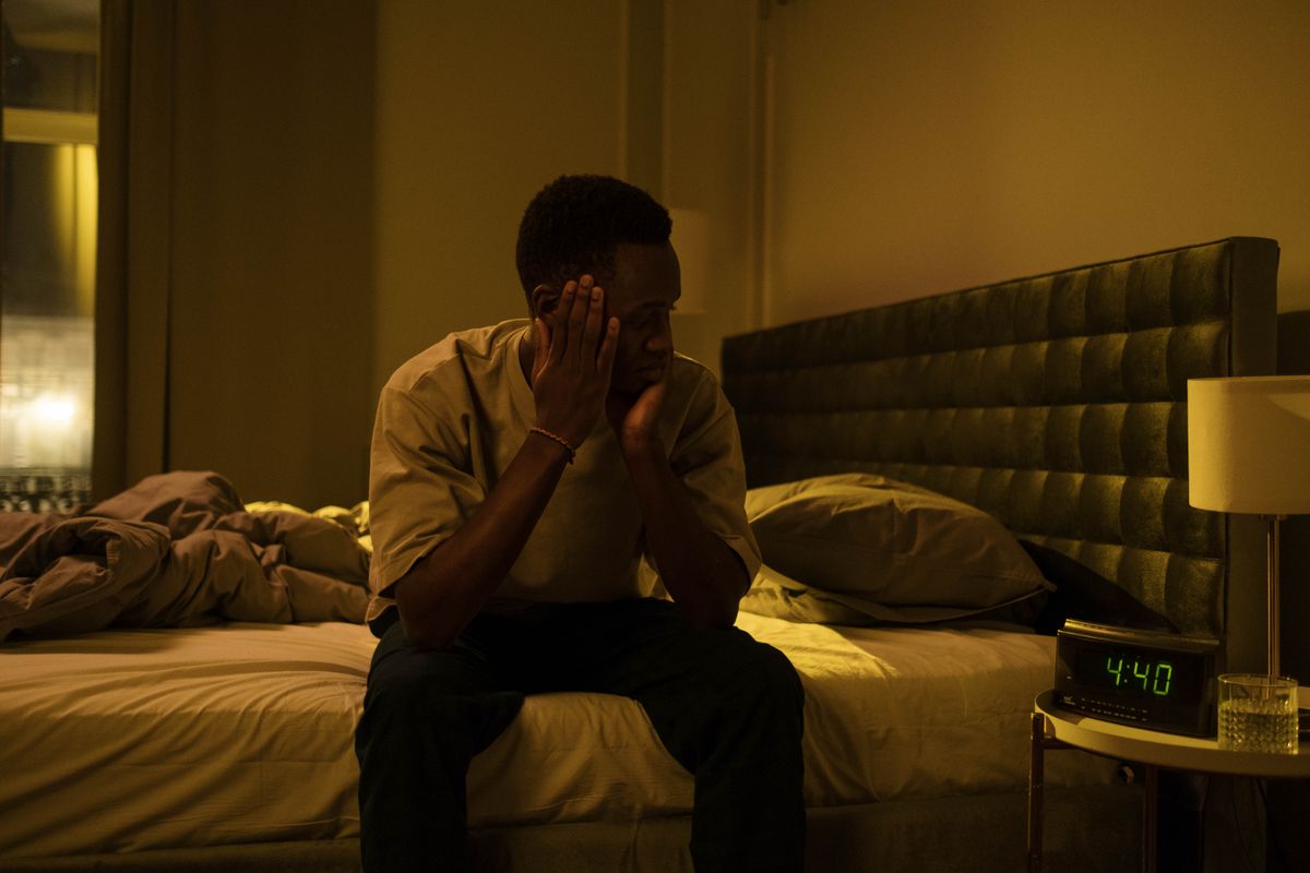 A tired man sitting awake on the edge of his bed at night, unable to sleep, the kind of patient a sleep apnea clinic wants to reach