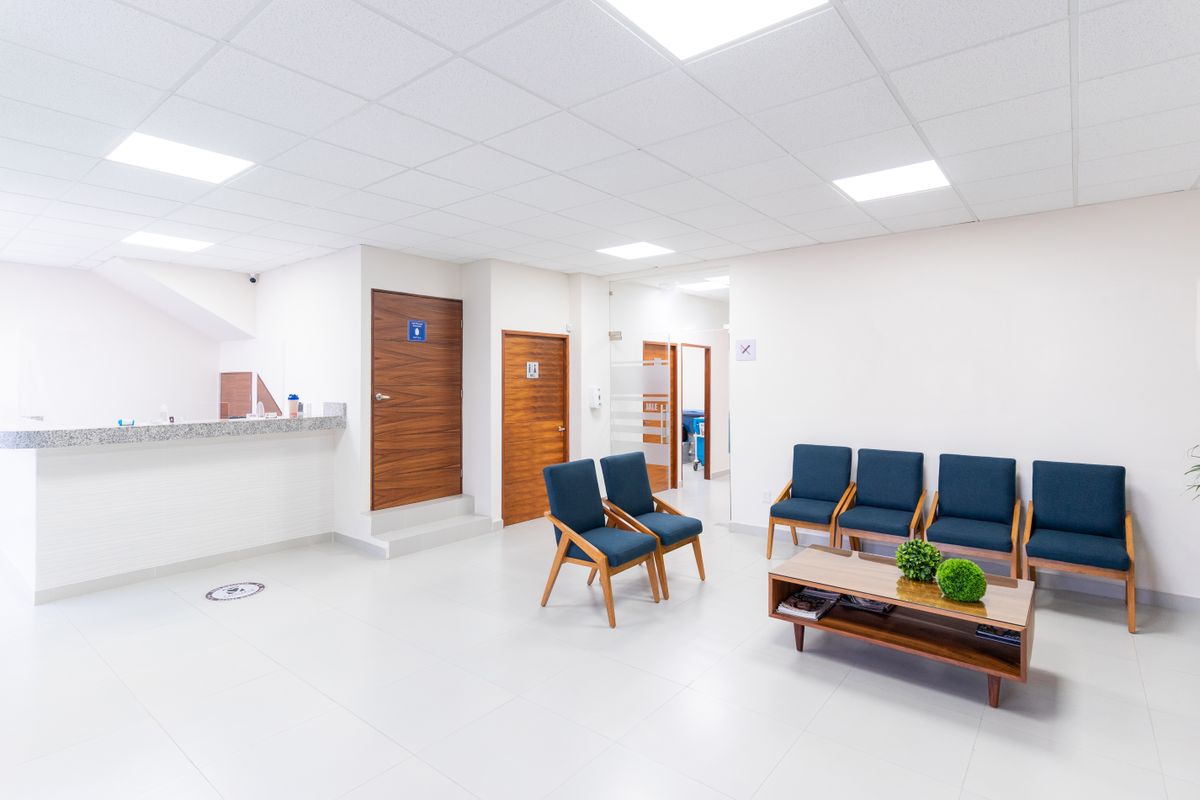 A clean, modern medical practice waiting room with blue chairs and a front desk, the captive space most practices leave empty of any marketing