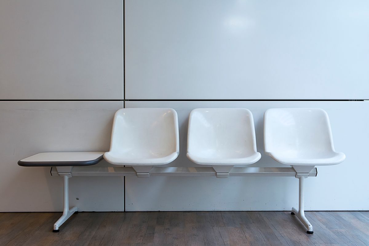 Three empty white chairs in a bright medical waiting room, the visible cost of a patient no show
