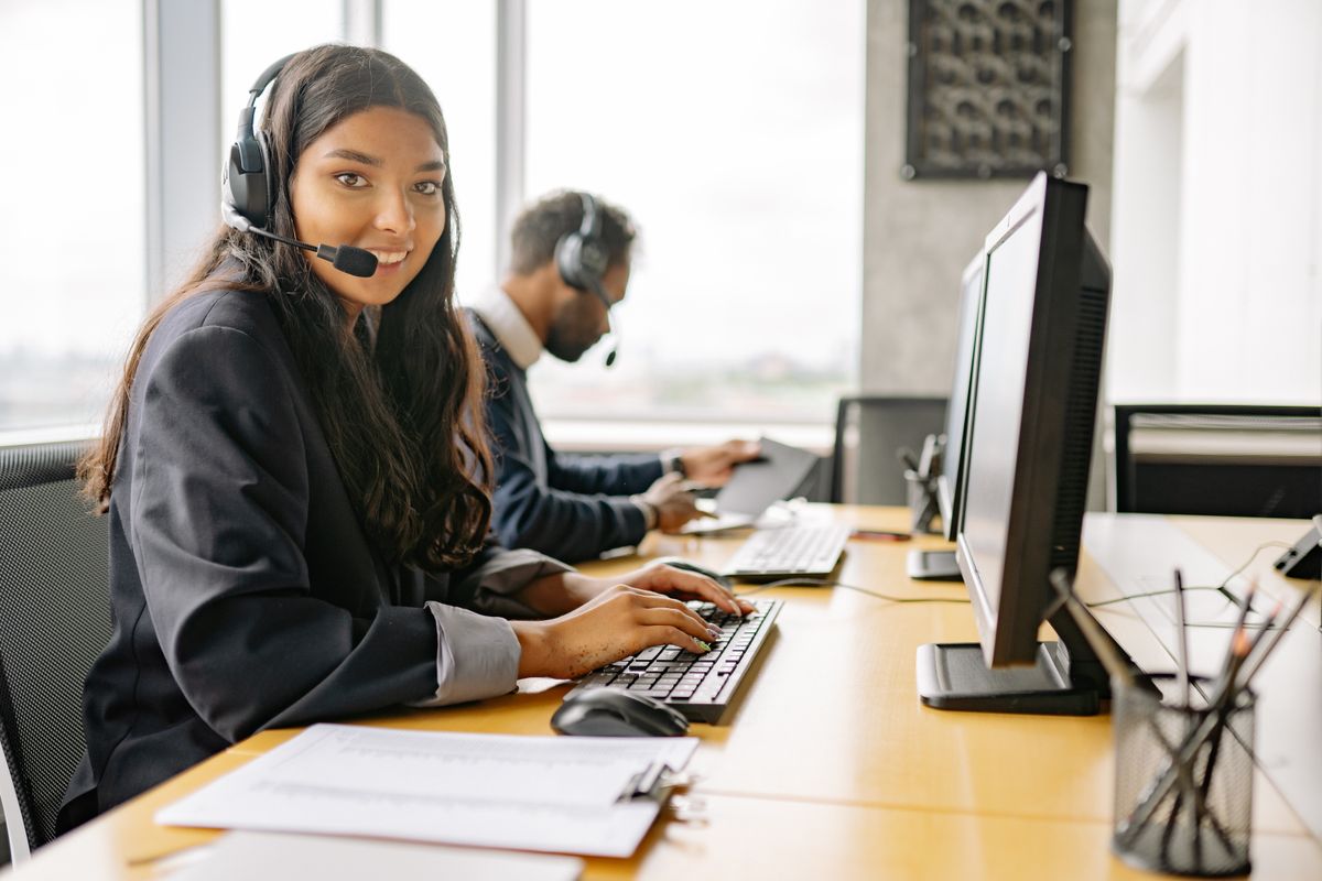 A friendly front desk team member with a headset at a computer, reaching out to welcome a new patient before their first visit