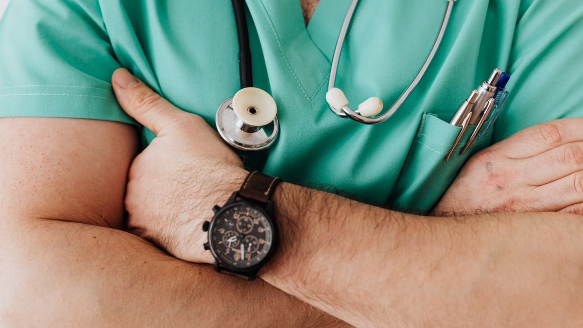 A doctor in green scrubs with a stethoscope and arms crossed, the kind of provider a new patient is trying to find online