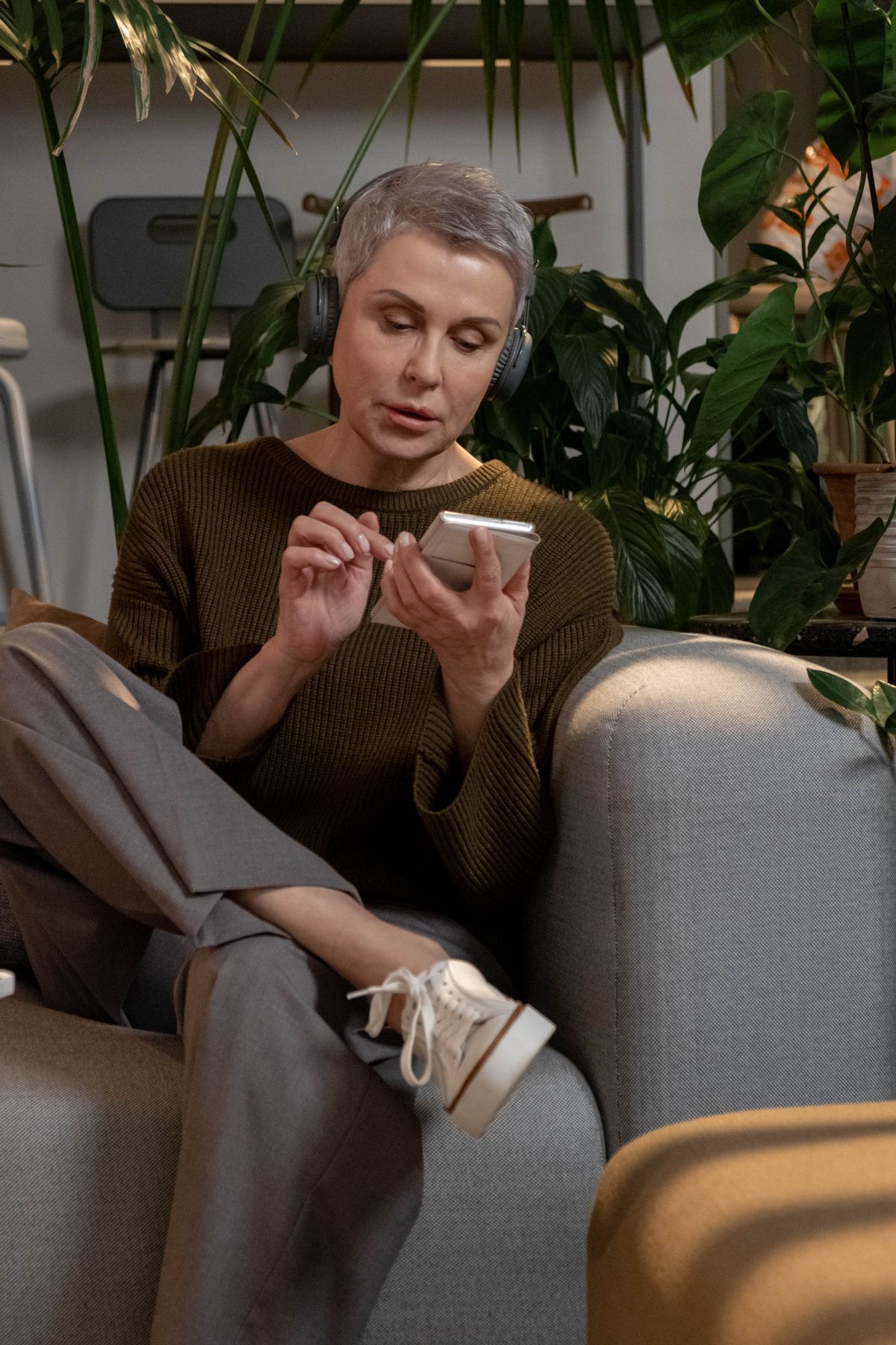 A middle aged woman sitting on a sofa using her smartphone to research and find a doctor online