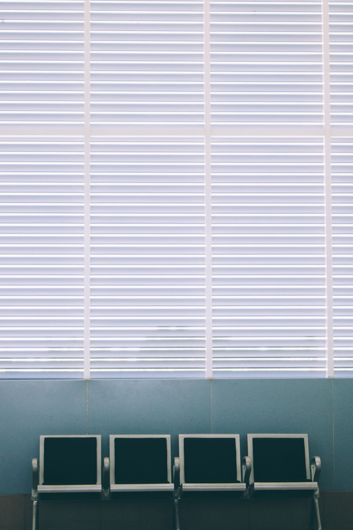 A row of four empty chairs in a medical practice waiting room with sunlight through window blinds, representing patient no shows