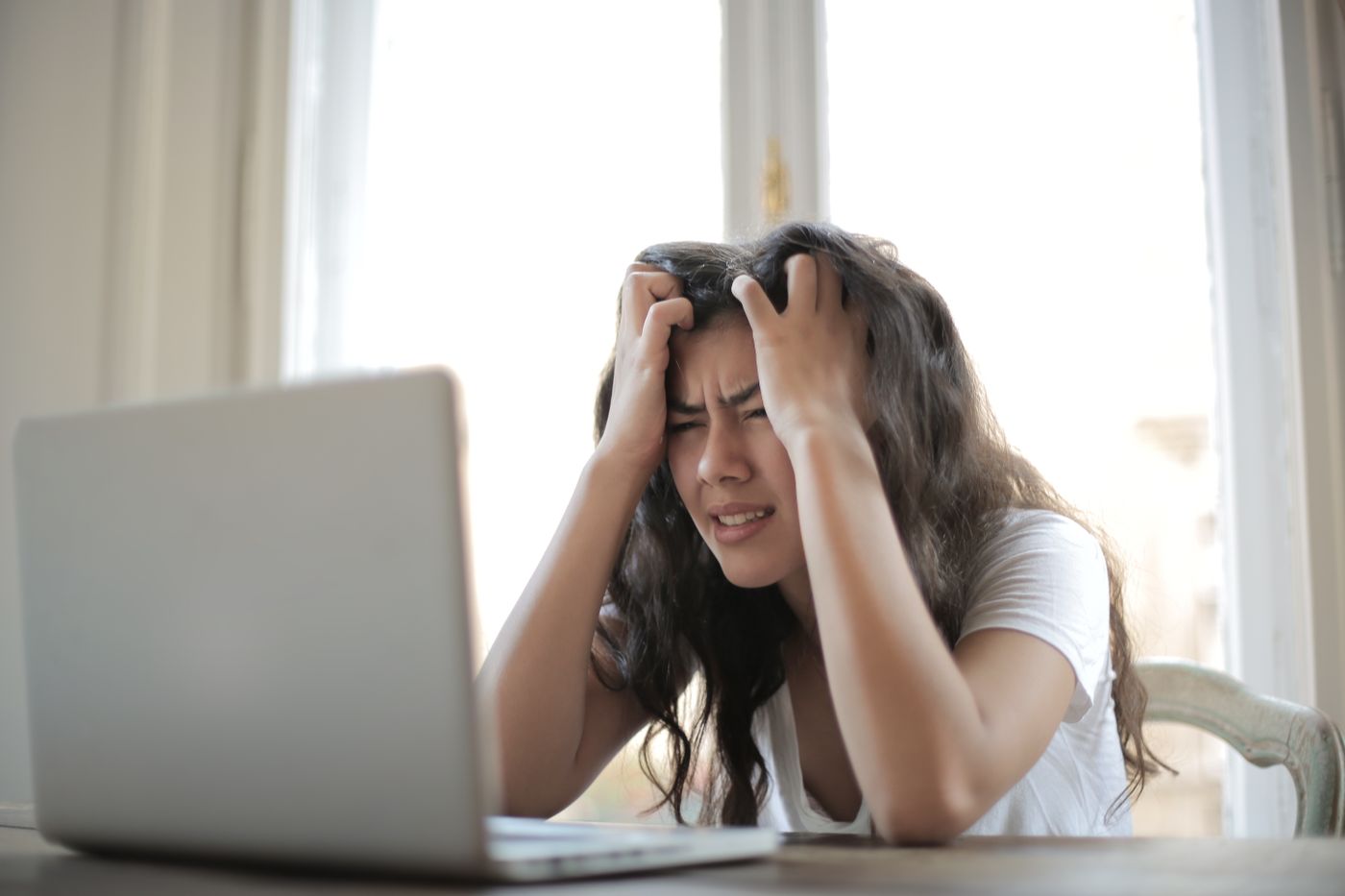 A frustrated medical practice owner holding her head while looking at a laptop, dealing with low quality fake ad leads