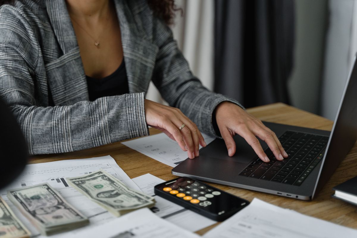 Person at a laptop with cash, a calculator, and financial reports, reviewing where a medical practice Google Ads budget is being spent