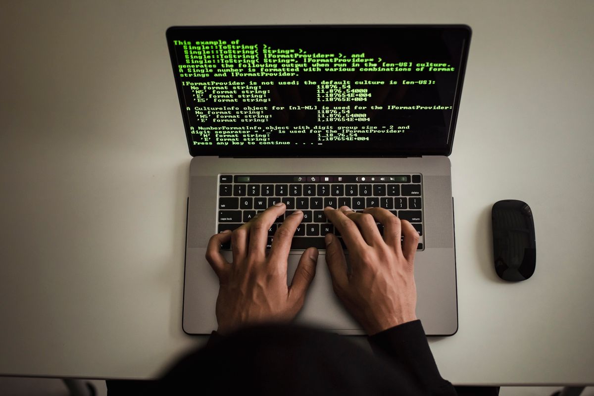 Hands typing on a laptop running automated scripts, the kind of bot that sends fake appointment requests to a medical practice booking form