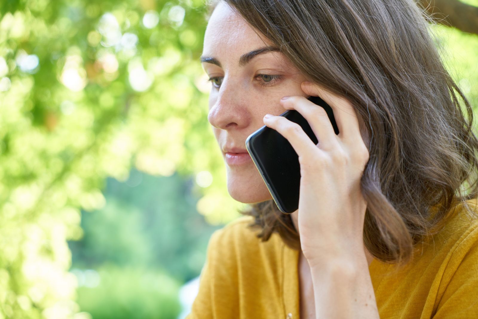 A woman looking unsure at an incoming call on her phone, deciding whether to answer a number labeled Spam Likely