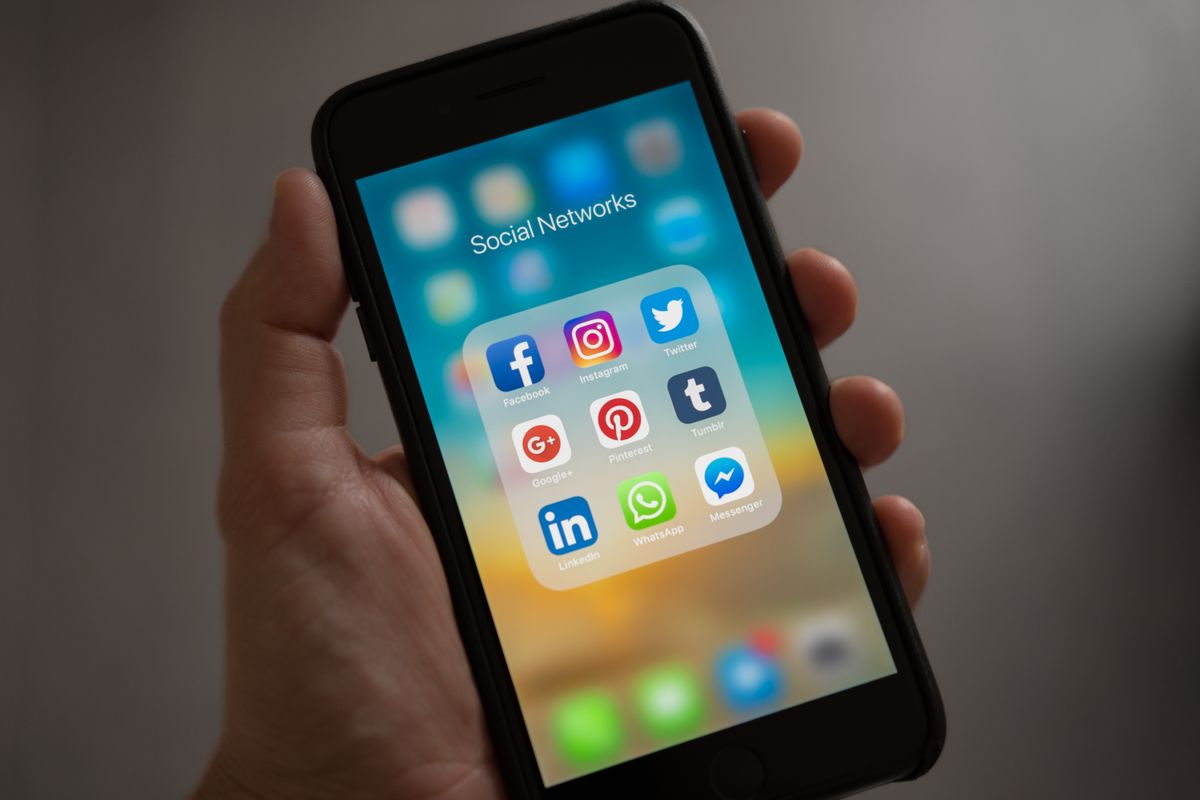 A hand holding a phone showing Facebook, Instagram, and other social media apps, where a medical practice's posts compete for reach