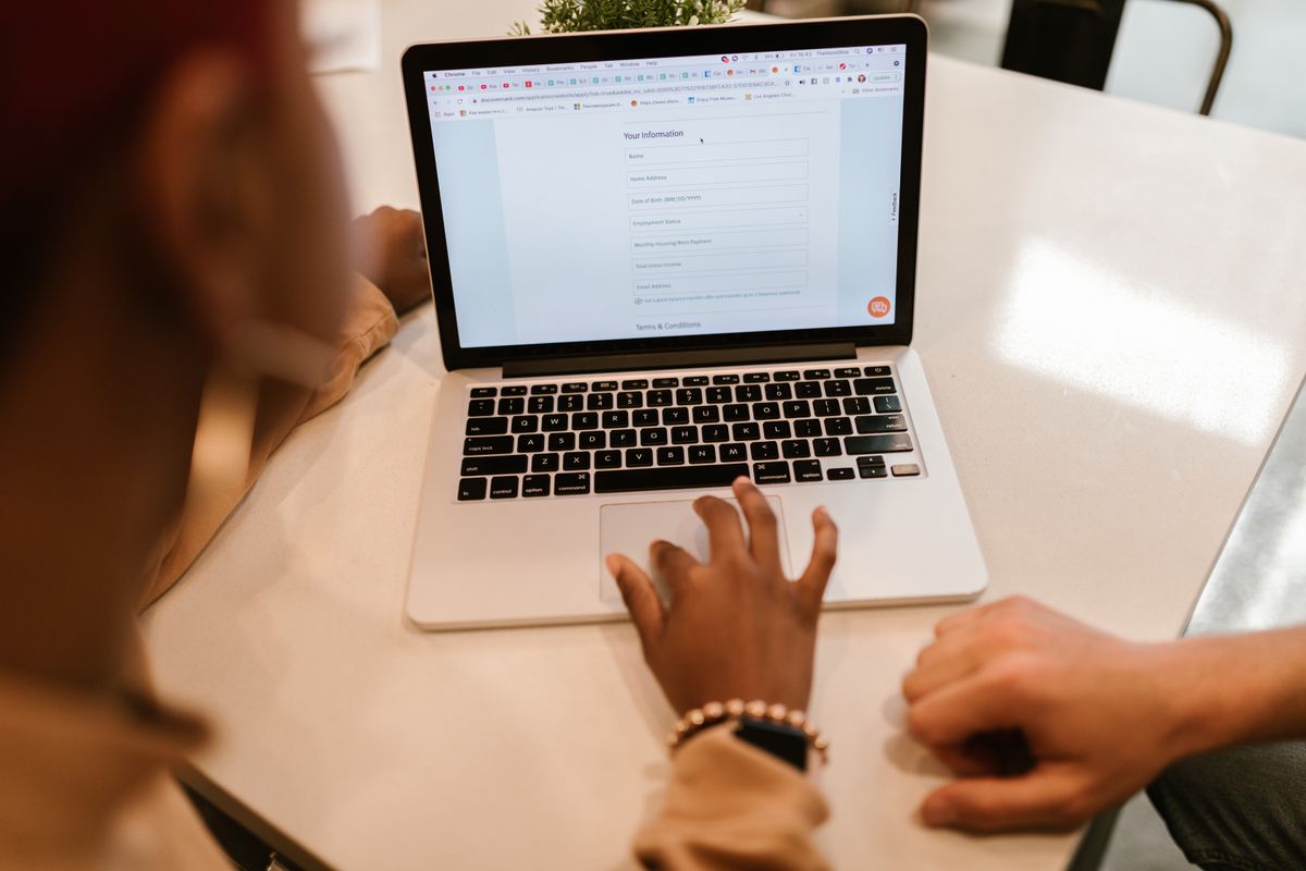 A patient on a laptop facing a long online form asking for name, address, date of birth, income and more, the kind of form that makes people quit before booking