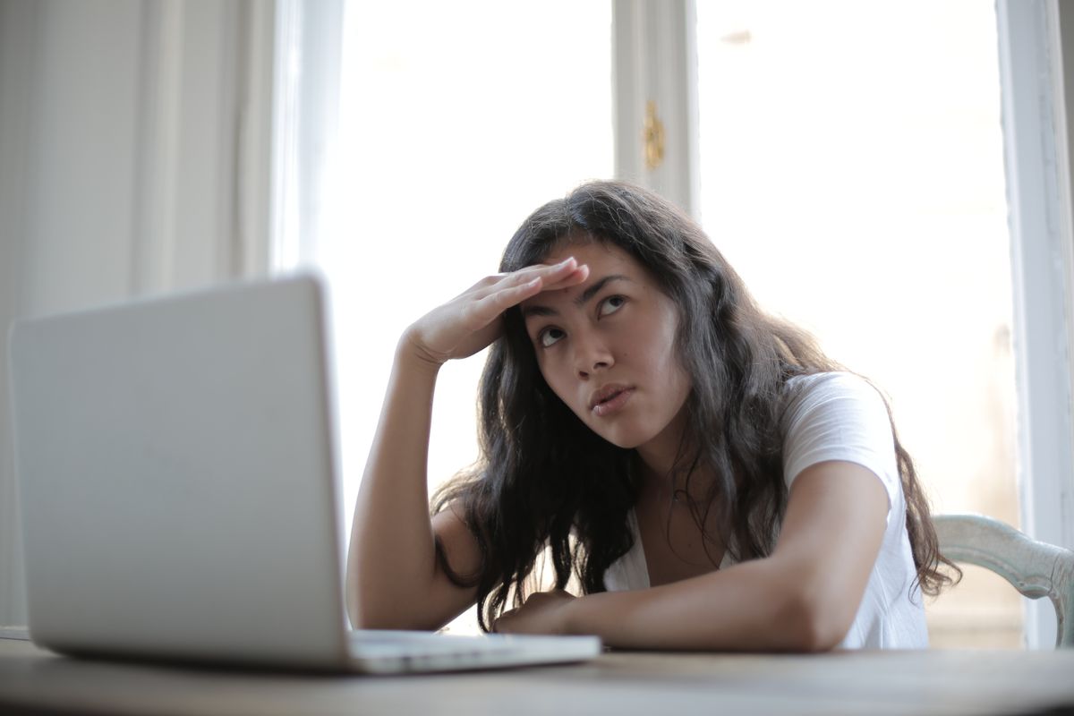 A patient sitting at a laptop looking uncertain while comparing doctors online before deciding who to book