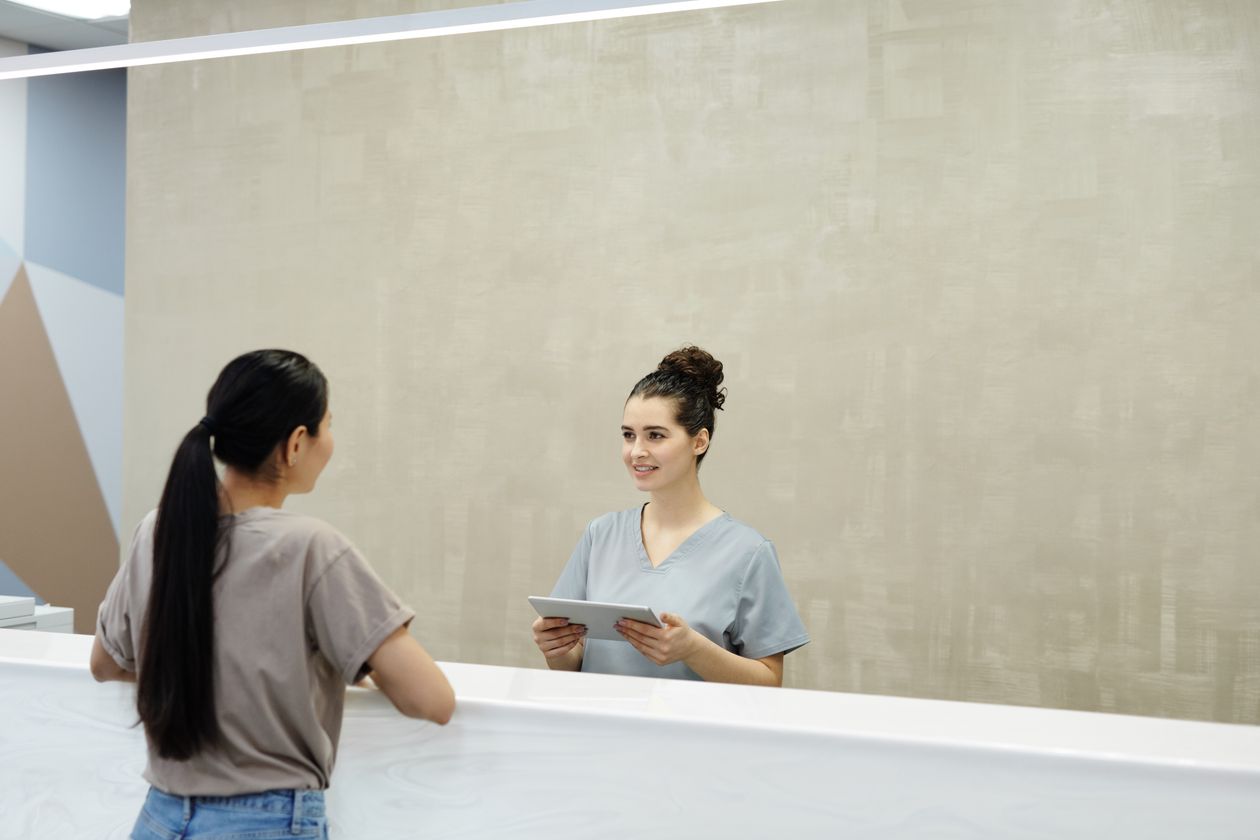 Medical front desk staff member helping a new patient, representing where practices catch or lose new patient leads