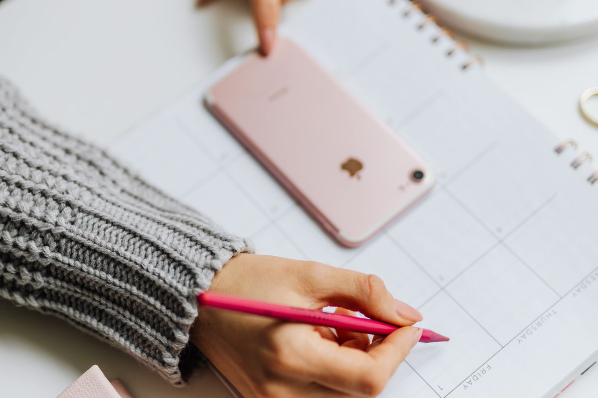 A patient holding a phone next to a weekly planner, about to book a medical appointment online
